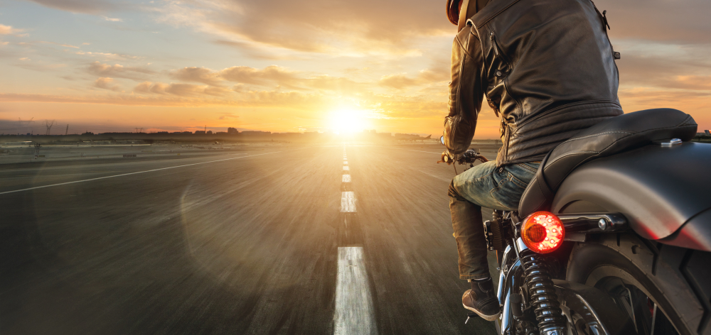 Motorcyclist on highway driving toward sunrise