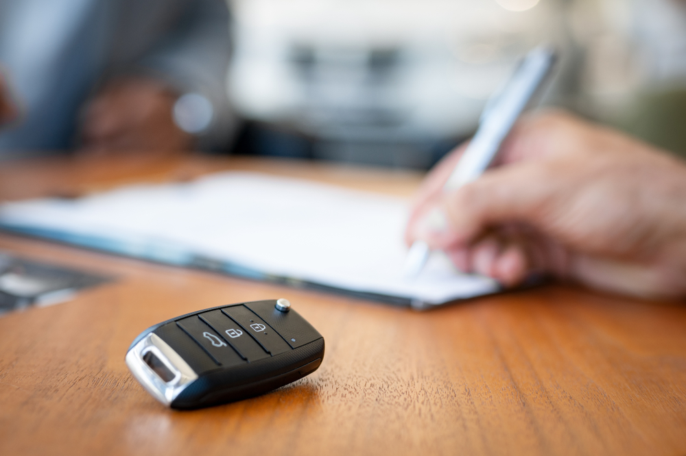 close up of hand signing lease agreement with car keys in foreground